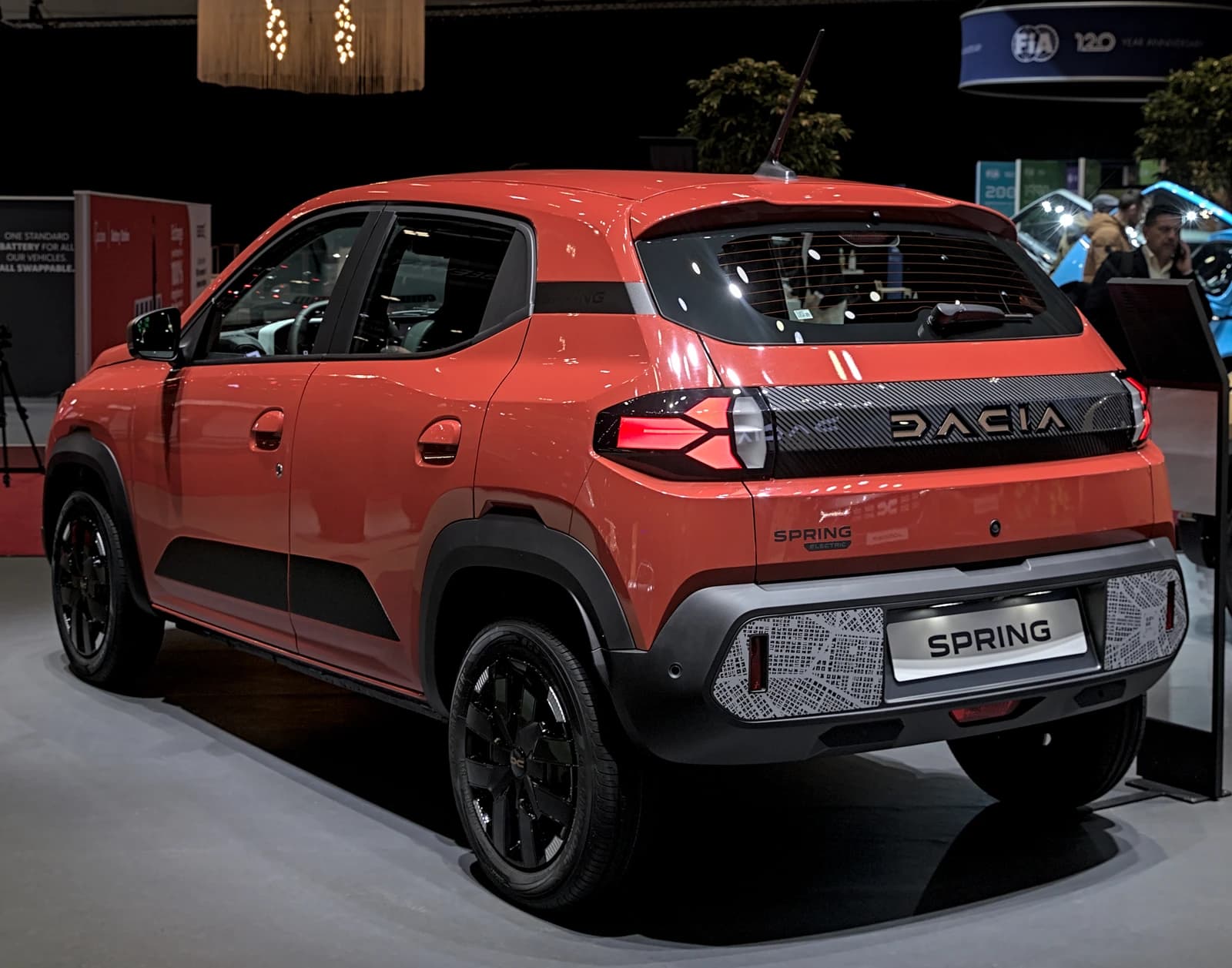 Rear view of an orange Dacia Spring Extreme electric car at an auto show.