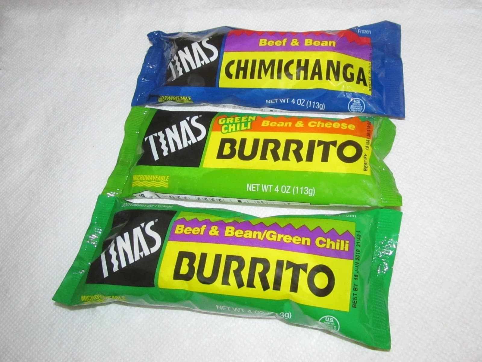 Three Tina's brand frozen burritos and a chimichanga in their packaging.