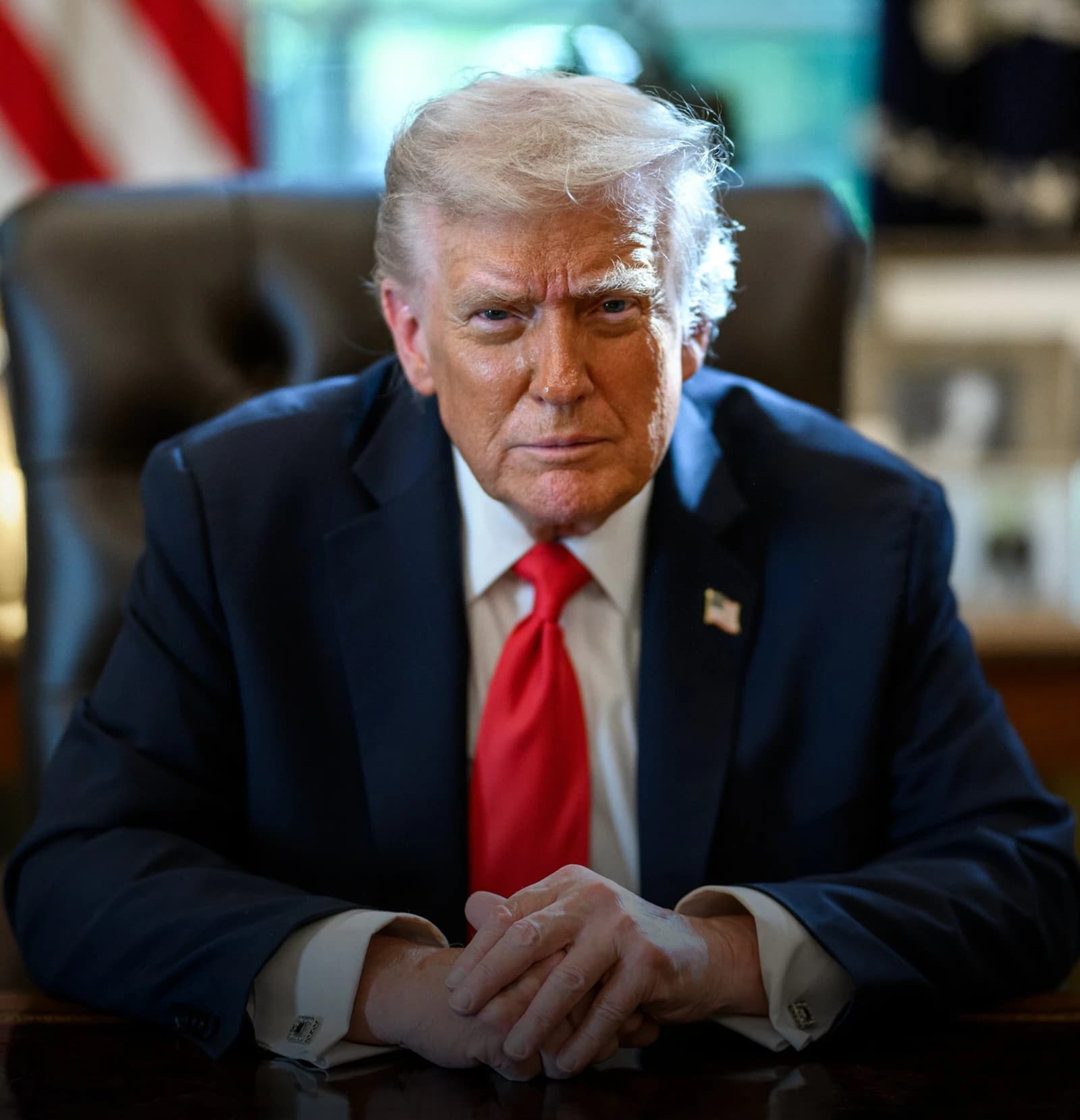 Donald Trump, former U.S. President, sitting at a desk in what appears to be the Oval Office.