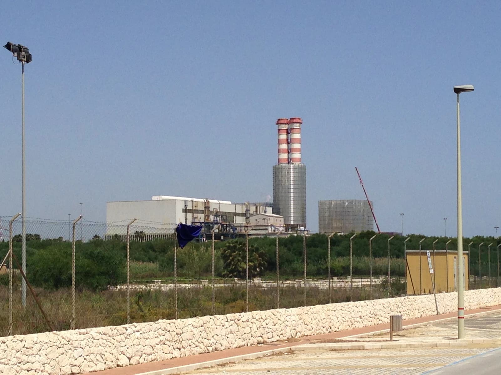 Archimede power plant in Syracuse, Italy, featuring two tall striped smokestacks and industrial buildings.