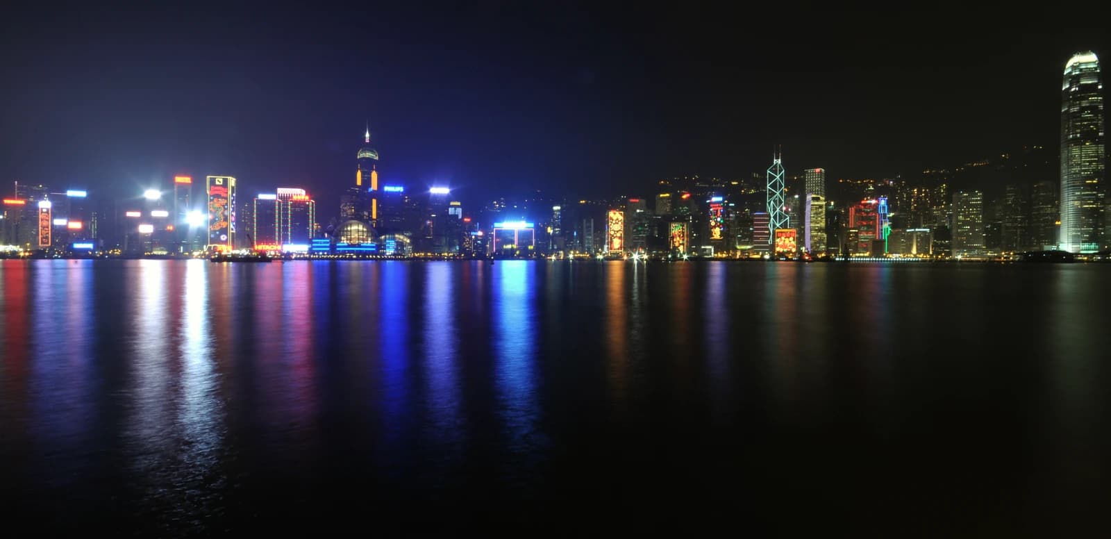 Hong Kong skyline at night with illuminated skyscrapers reflecting in Victoria Harbour.