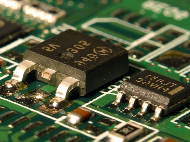 Close-up of small black computer chips soldered onto a green circuit board.