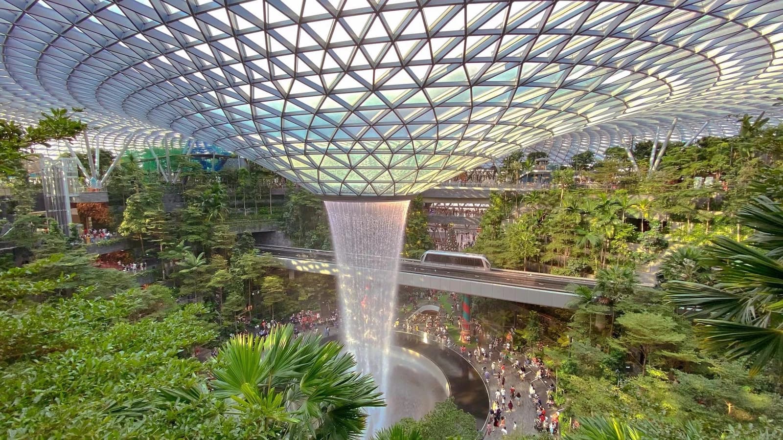 People walking around the indoor Rain Vortex waterfall at Jewel Changi Airport in Singapore.
