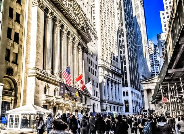 People walking outside the New York Stock Exchange building under a blue sky.