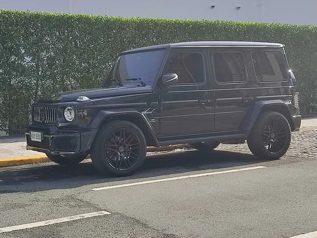 Black Mercedes-Benz G-Wagen Brabus parked on a street with a green hedge behind it.