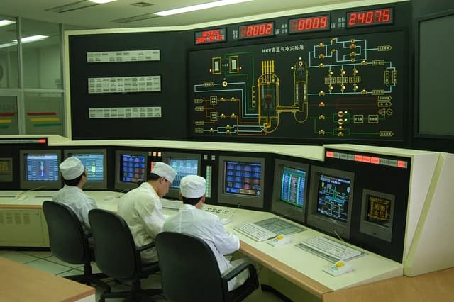 Engineers monitor control screens and a schematic diagram of a nuclear reactor.