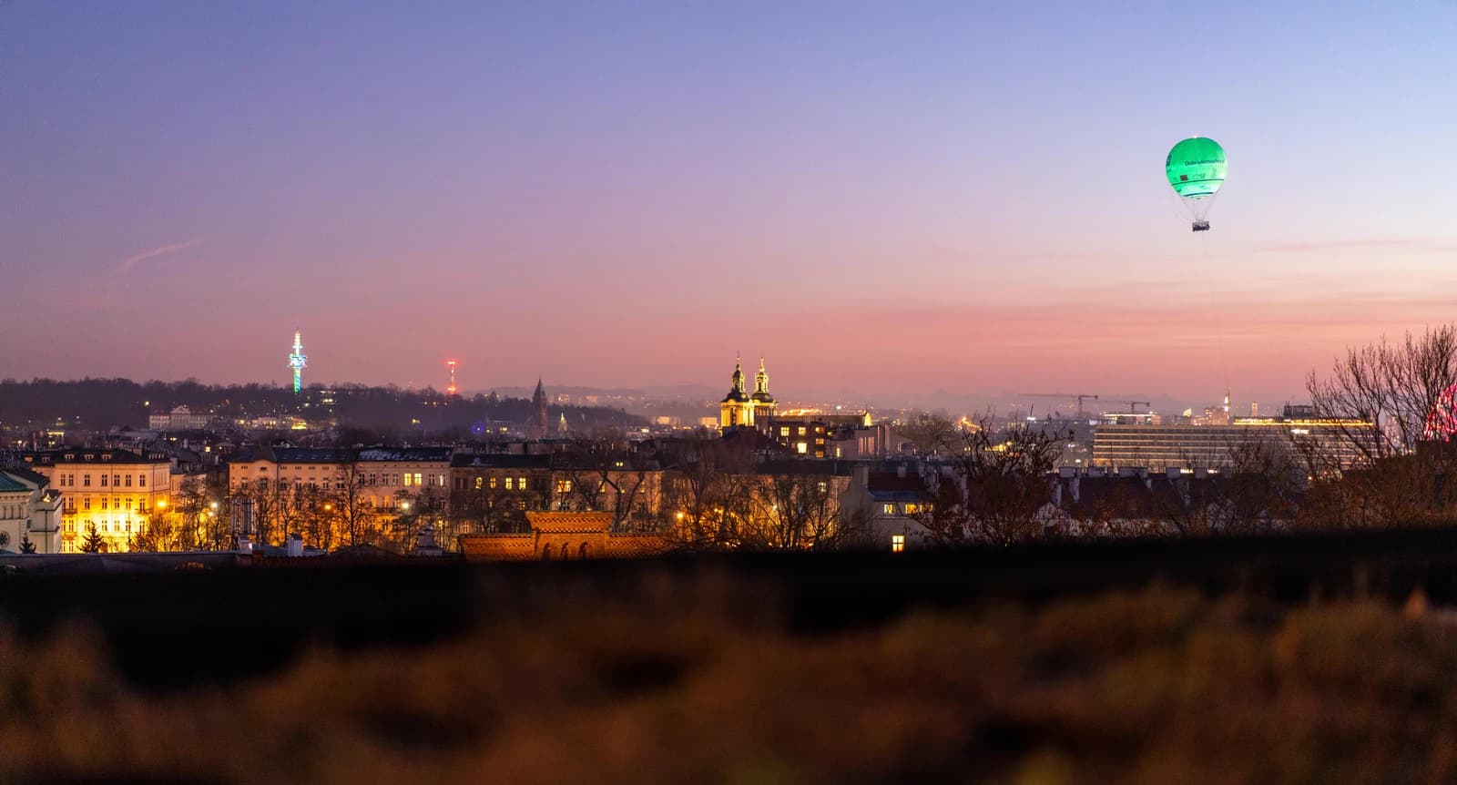Kraków cityscape at sunset with a green hot air balloon in the sky.