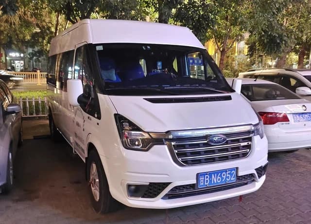 White Ford Transit Pro van parked on a sidewalk at night, with streetlights visible.