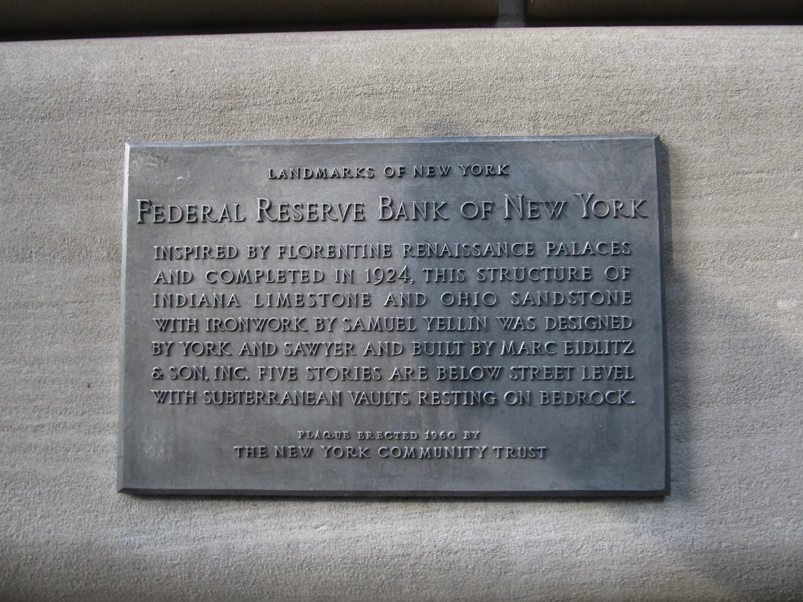 Plaque on a stone wall detailing the history of the Federal Reserve Bank of New York.