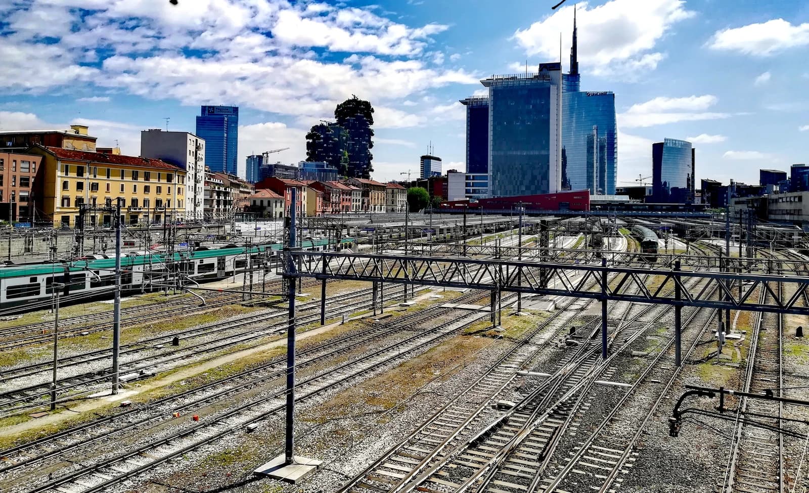 Milan's Porta Garibaldi railway station tracks in foreground, with city skyline and financial buildings behind.