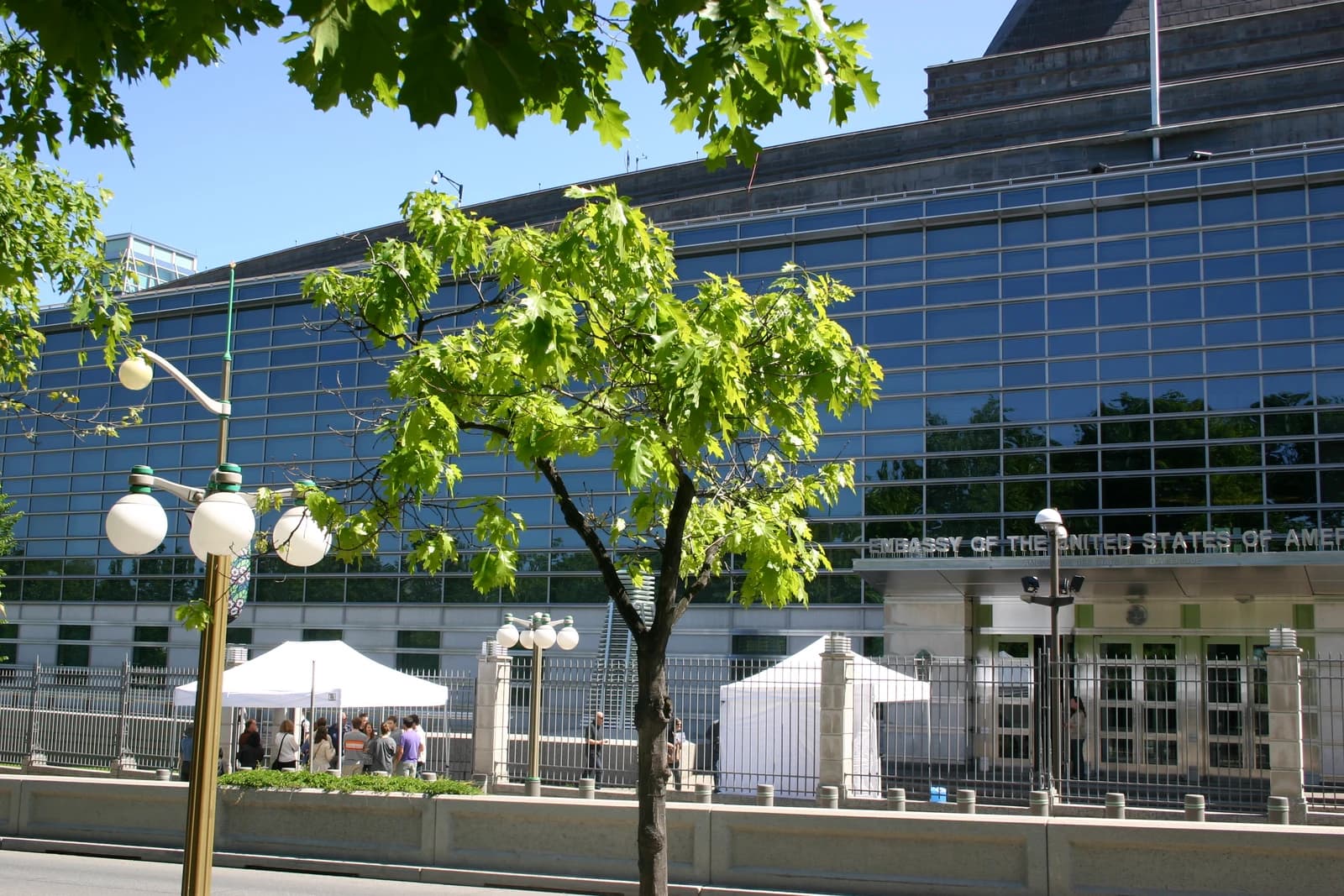 Exterior of the US Embassy building with trees and people outside.