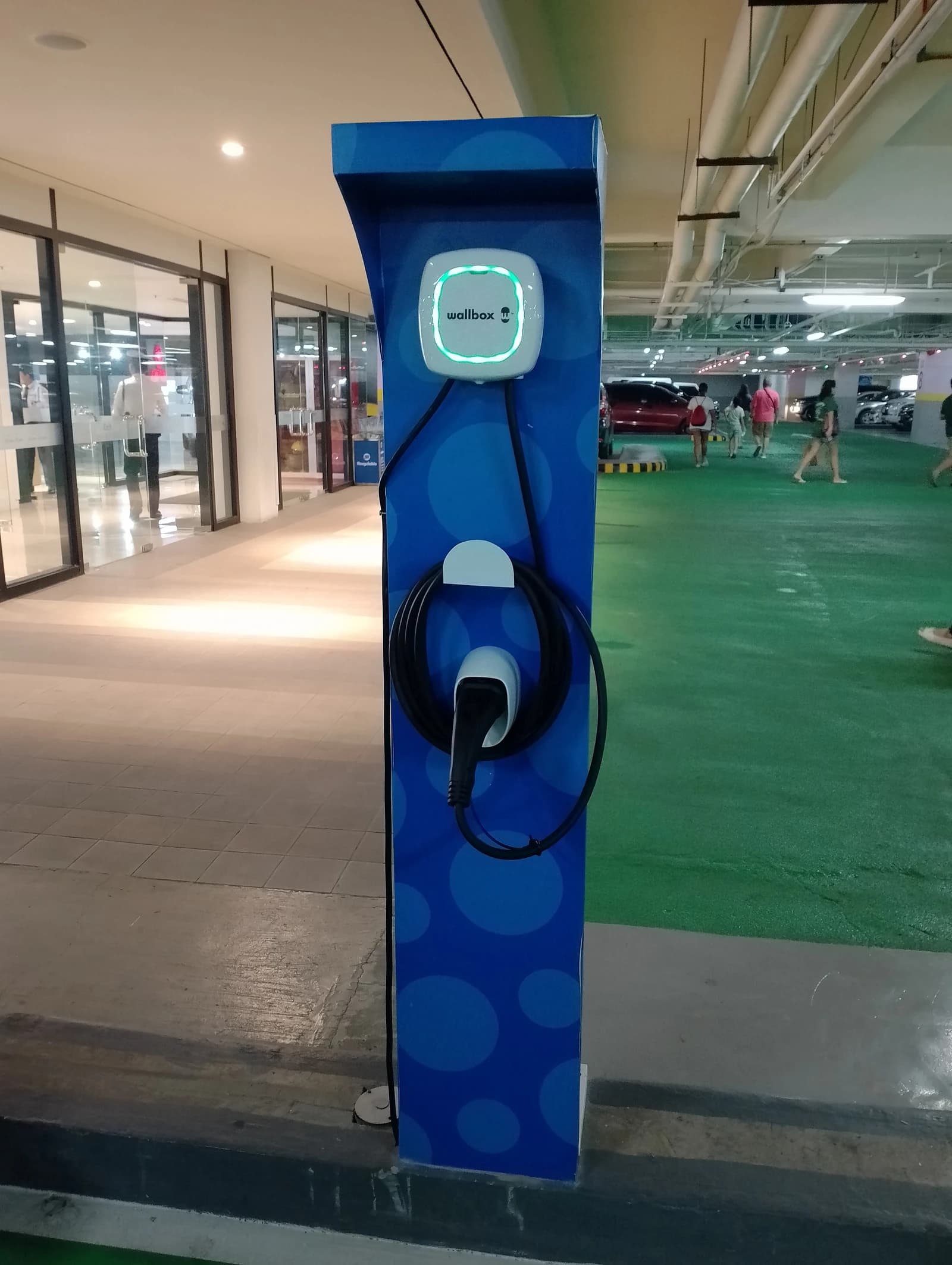 Wallbox EV charging station on a blue pedestal in a mall parking lot.