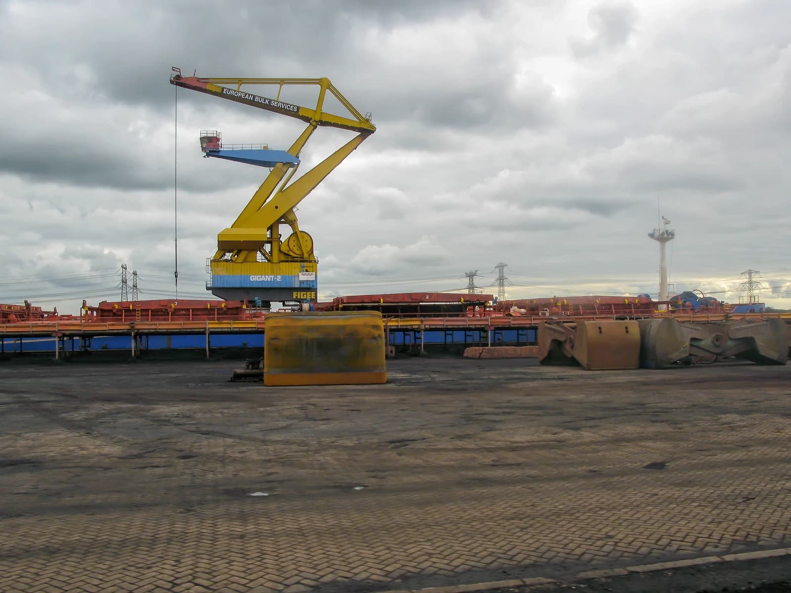 Large yellow bulk cargo crane with 'European Bulk Services' and 'Gigant-2' visible, under a cloudy sky.