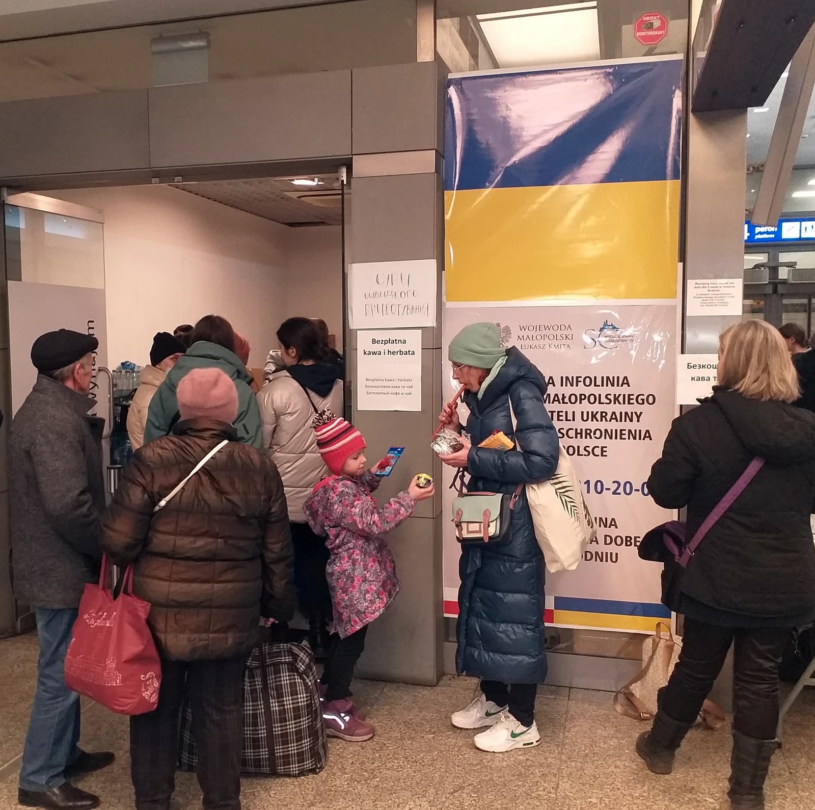 People gather at an aid station with a Ukrainian flag banner at a railway station.