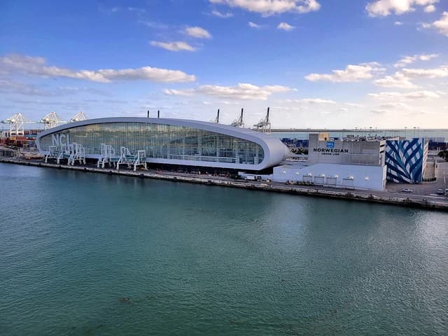 Norwegian Cruise Line Terminal B building at PortMiami, with cargo cranes in the background.
