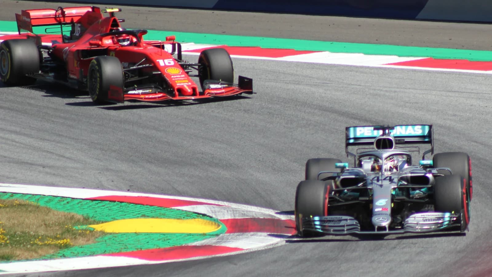 Lewis Hamilton in a Mercedes F1 car on a race track with another car.