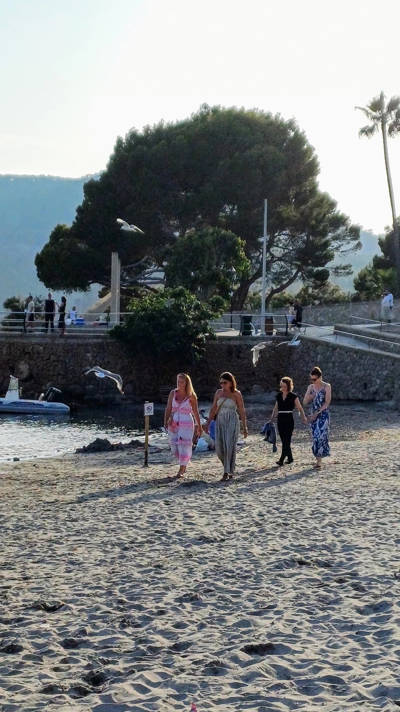 Four women walking along a sandy beach near the water's edge.
