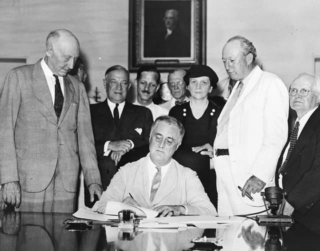 President Franklin D. Roosevelt signs the Social Security Act surrounded by officials.