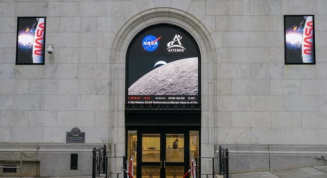 Exterior of building with large arched screen showing stock tickers and NASA Artemis Moon imagery.