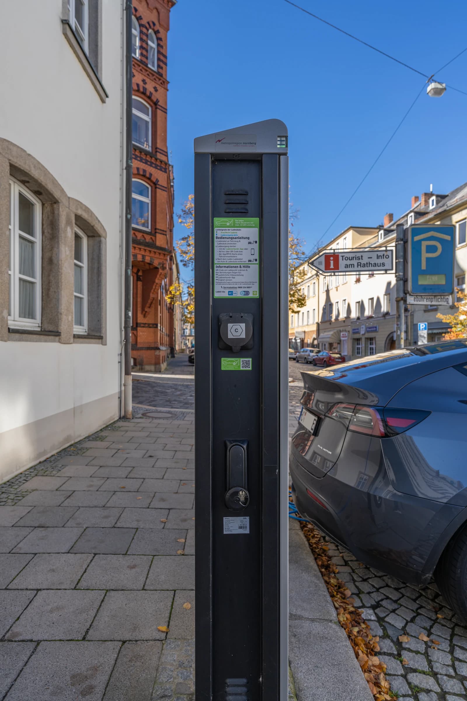 Gray Tesla electric car connected to a black charging station on a European street.