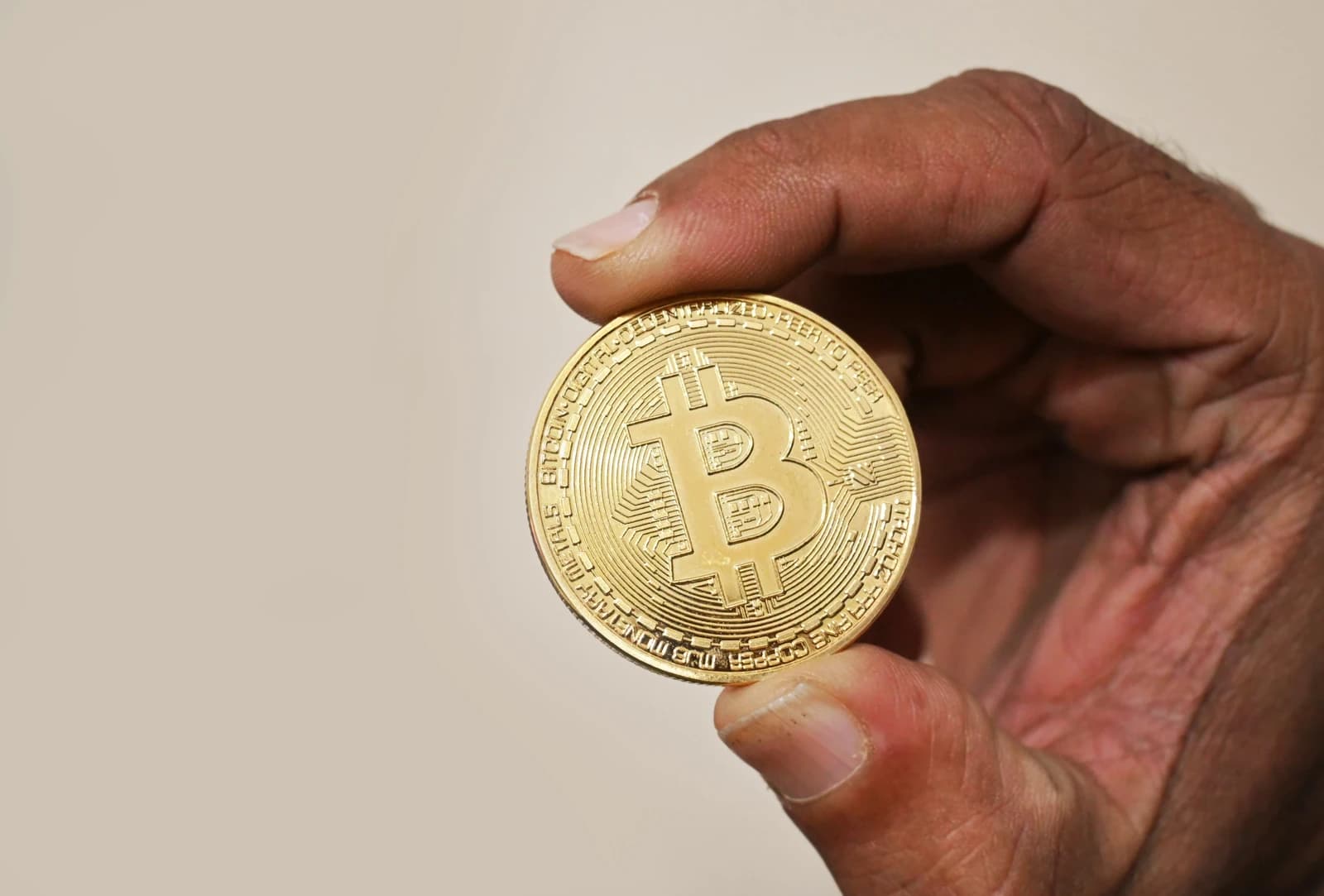 A hand holding a physical representation of a Bitcoin cryptocurrency coin.