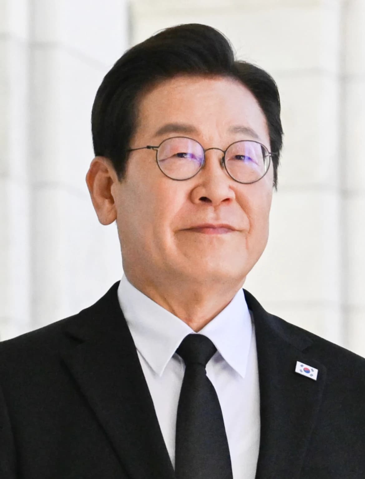 President Lee Jae-myung looking forward, wearing glasses and a suit with a flag pin.