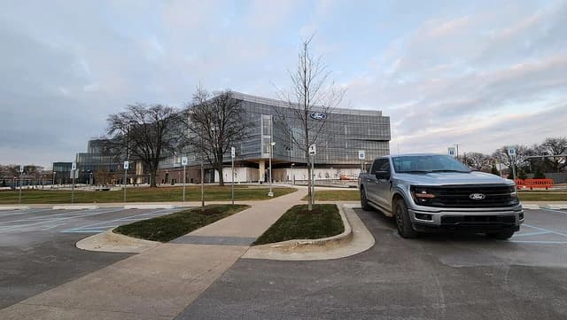 Ford World Headquarters building in Dearborn, Michigan, with a silver F-150 pickup truck.