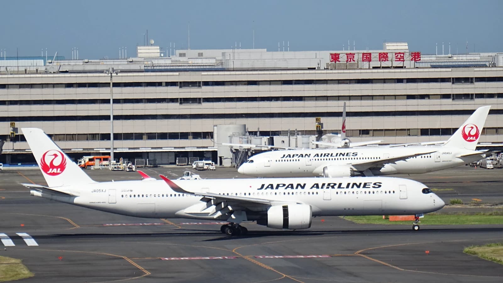 Two JAL Japan Airlines aircraft parked at Haneda Airport terminal building.