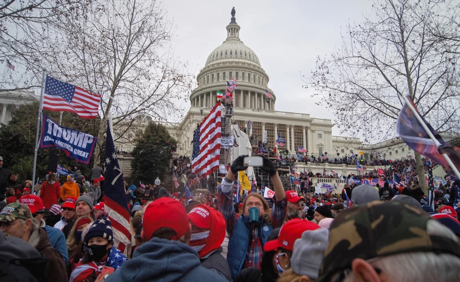 Crowd of people gathered outside the US Capitol building, some holding flags.