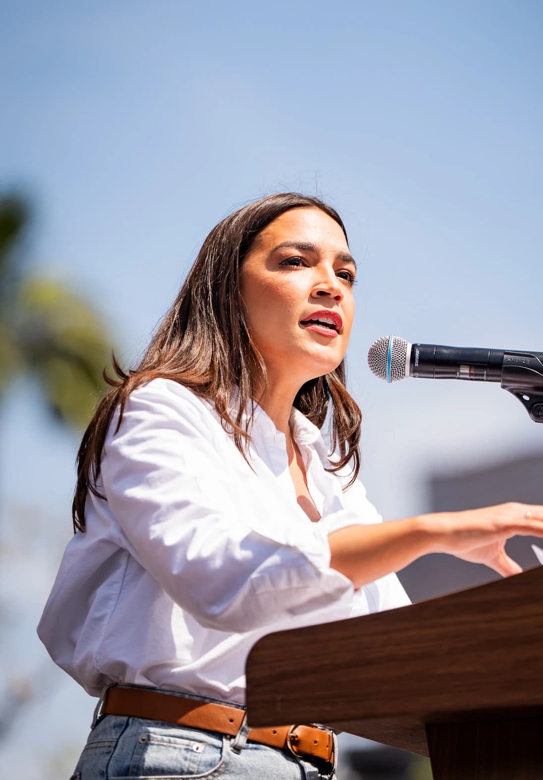Alexandria Ocasio-Cortez, US Representative, speaking at a podium with a microphone.