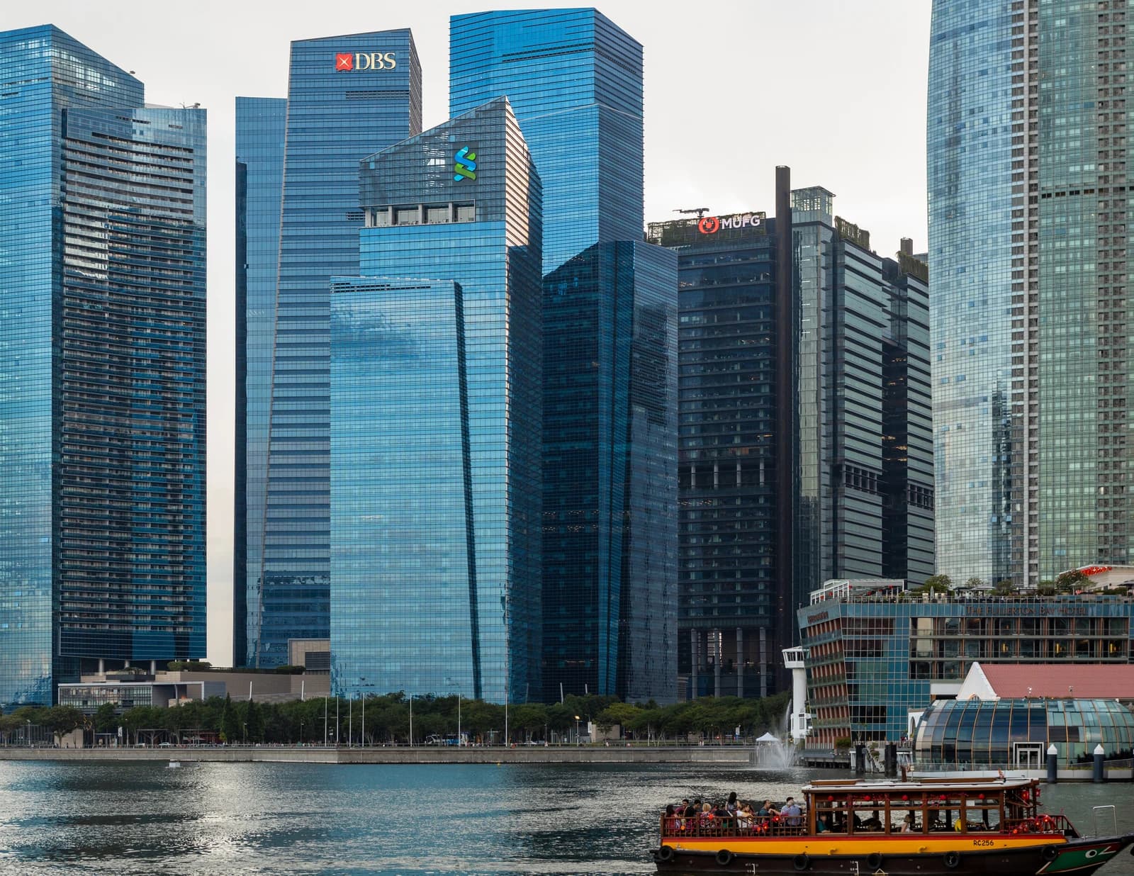 Singapore Downtown Core skyline with multiple modern high-rise buildings and a riverboat on the water.