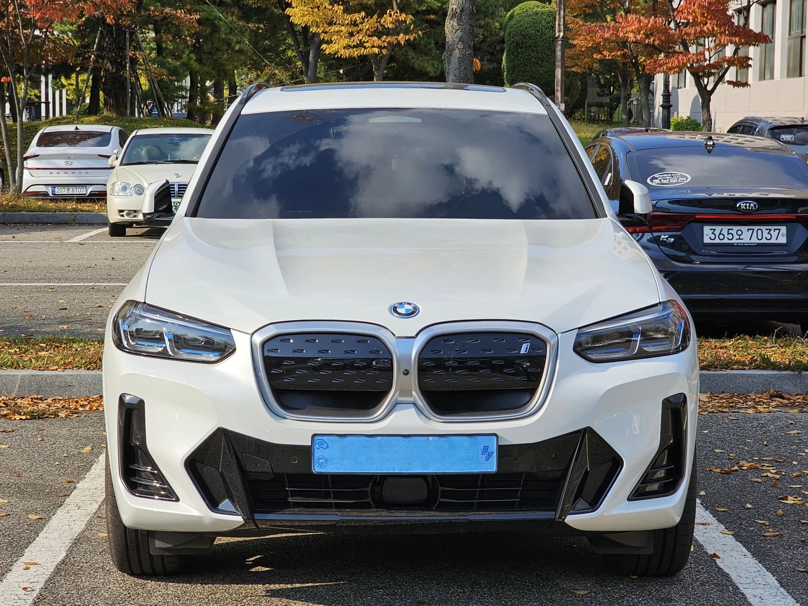 White BMW iX3 M Sport vehicle parked outdoors on a sunny day.