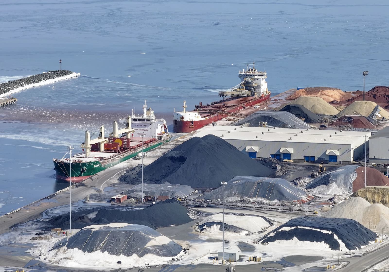 Two cargo ships docked at the Port of Belledune, surrounded by various material piles.