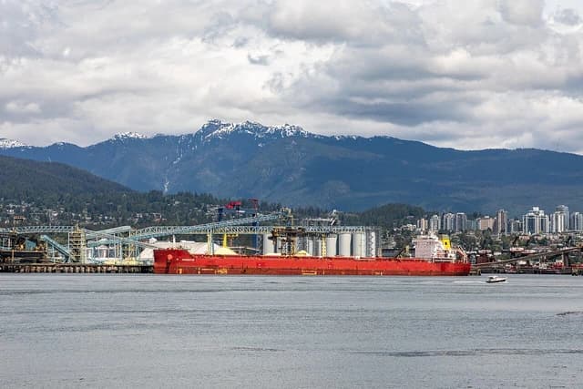 Large red cargo ship docked at Pembina Canada Terminals, Vancouver, with mountains behind.