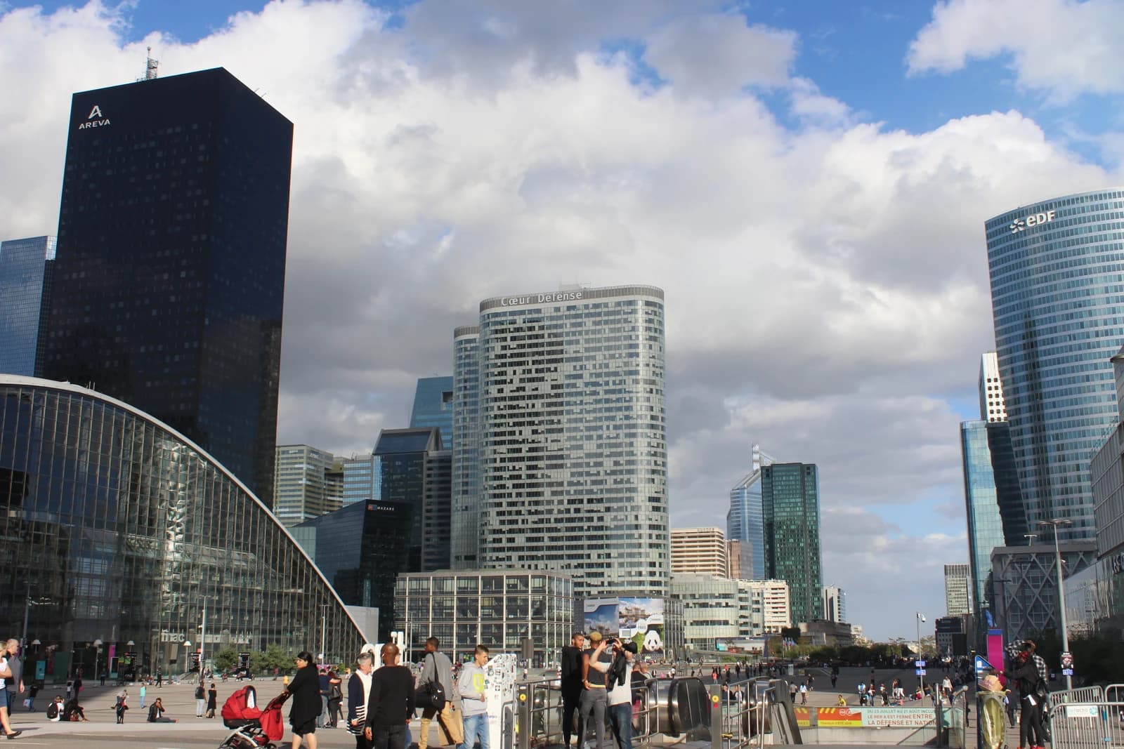 People walking on a large plaza in front of tall modern buildings in La Défense, Paris.