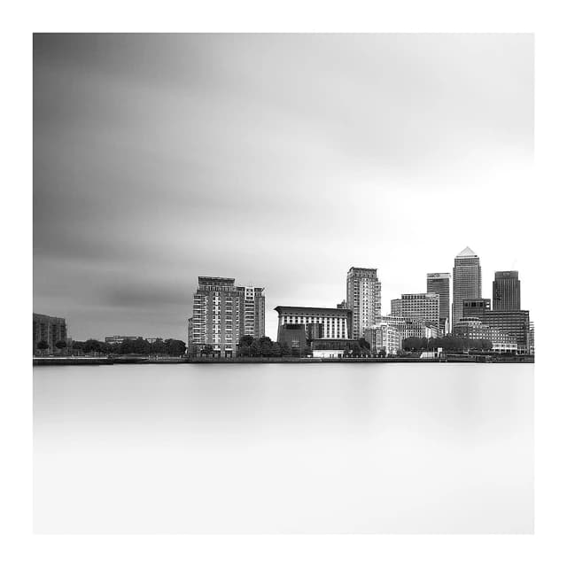 Black and white skyline of tall buildings in Canary Wharf reflected in water.