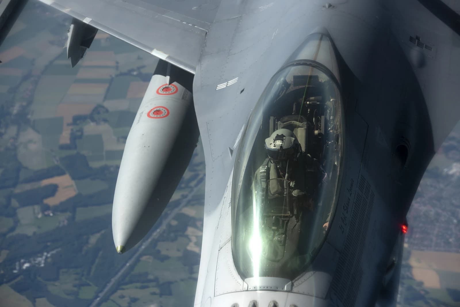 Pilot wearing a helmet and oxygen mask in the cockpit of a US Air Force fighter jet.