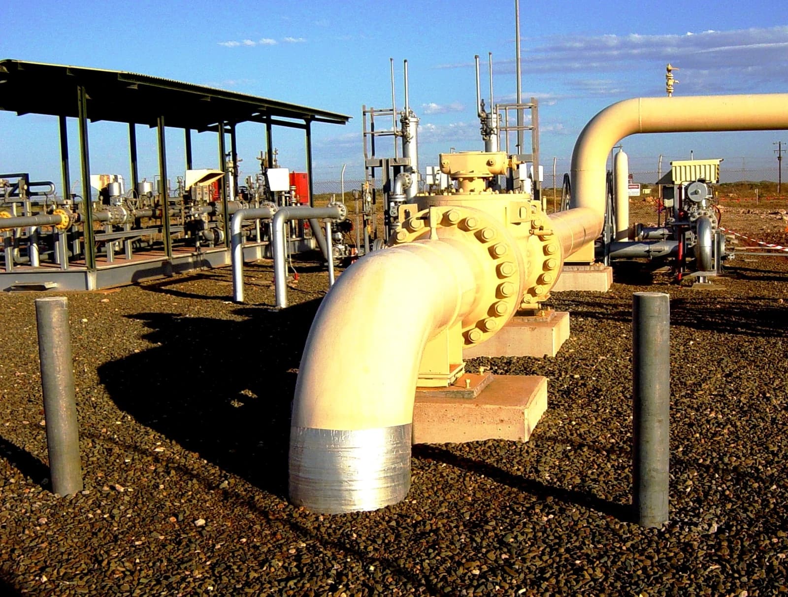 Natural gas pipeline station with large yellow pipes and equipment in an outdoor setting.