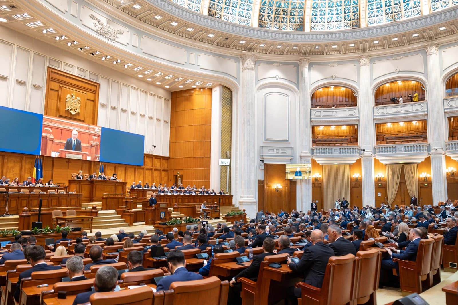 Ilie Bolojan, Romanian Prime Minister, speaking at a podium in a large assembly hall.