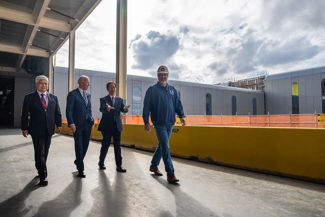 Joe Biden, Mark Liu, Morris Chang, and a construction worker walk outdoors at a facility.
