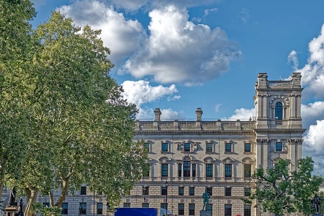 Exterior of the HM Treasury building in Westminster, London, under a blue sky.