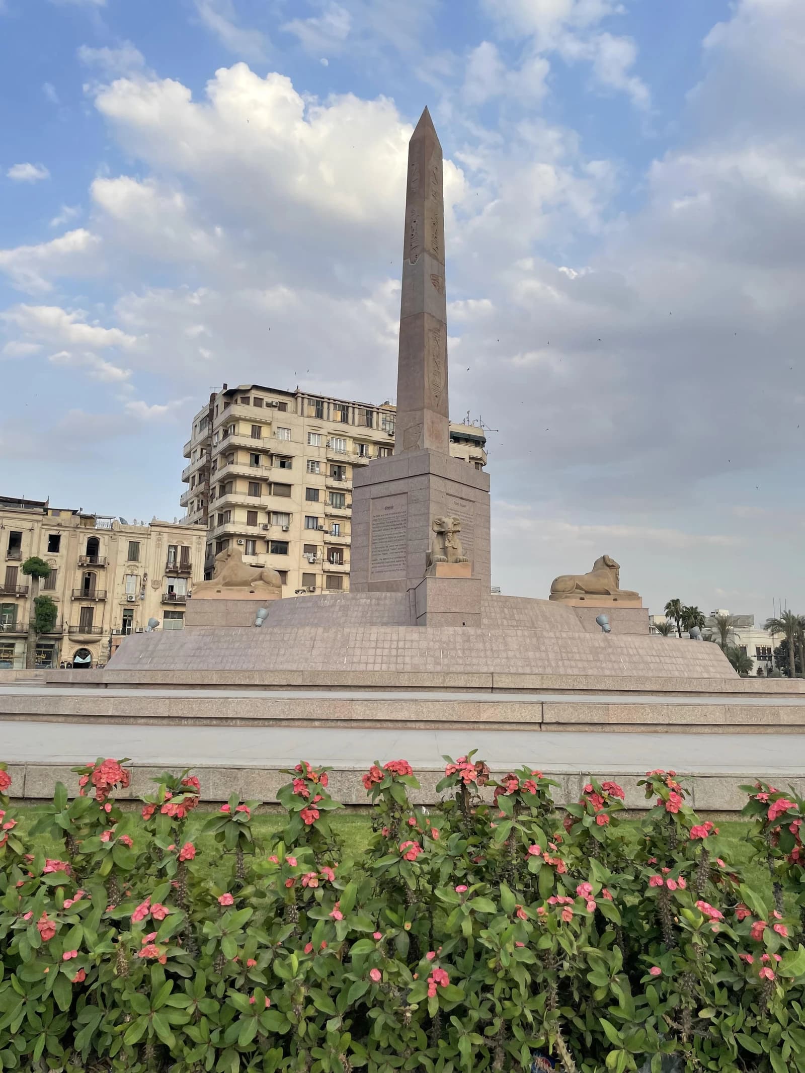 Obelisk monument and sphinx statues in Tahrir Square, Cairo, Egypt, under a cloudy sky.