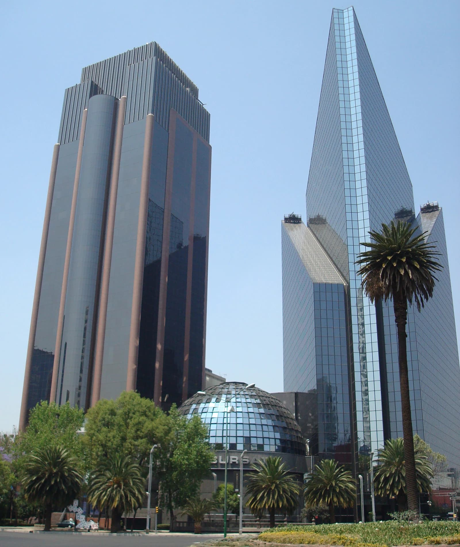 The Bolsa Mexicana de Valores (Mexican Stock Exchange) building, a glass dome, with tall modern skyscrapers in the background.