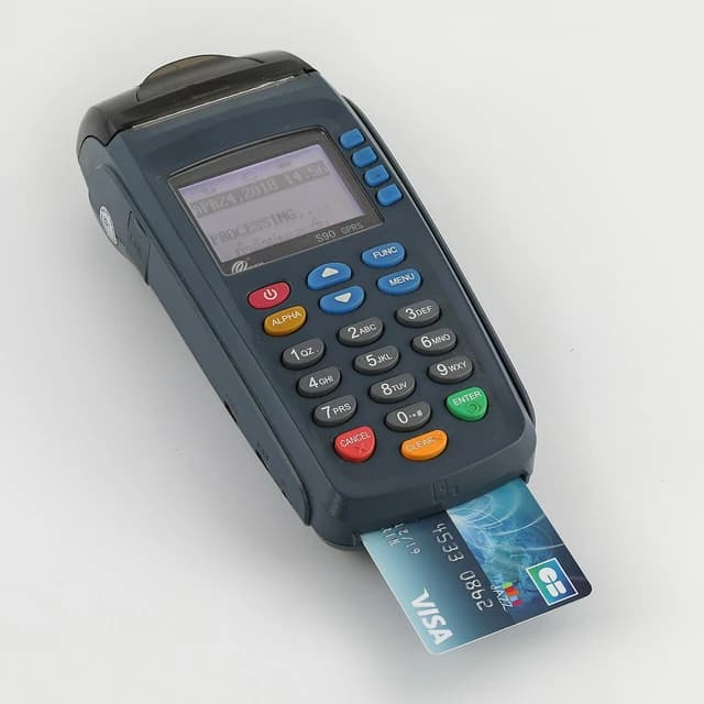 A Visa credit card inserted into a payment terminal displaying "PROCESSING".