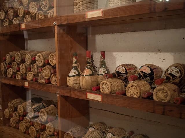 Wine cellar with many bottles of wine wrapped in straw on wooden shelves.