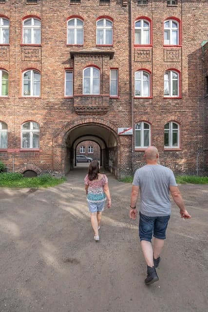 Two people walk away from the viewer into an arched passage of a brick building.