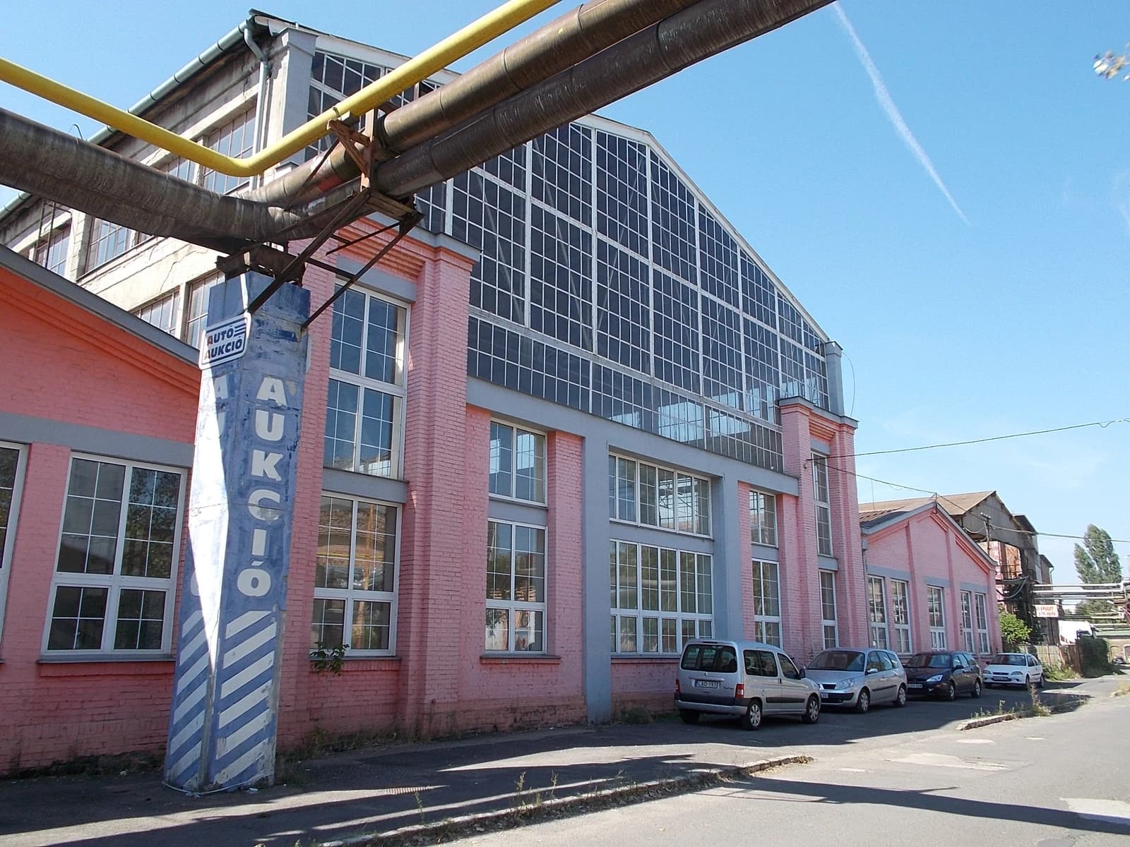 Industrial building with a large glass facade and a blue pillar labeled 'Autó Aukció'.