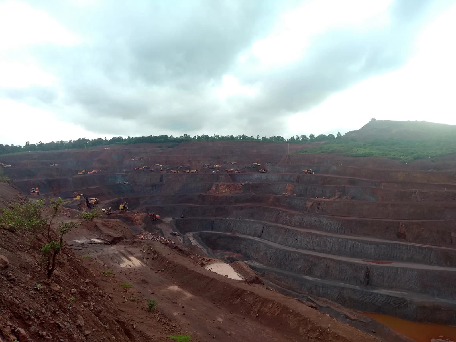 Overview of large-scale open-pit iron ore mine with multiple terraced levels and mining equipment.