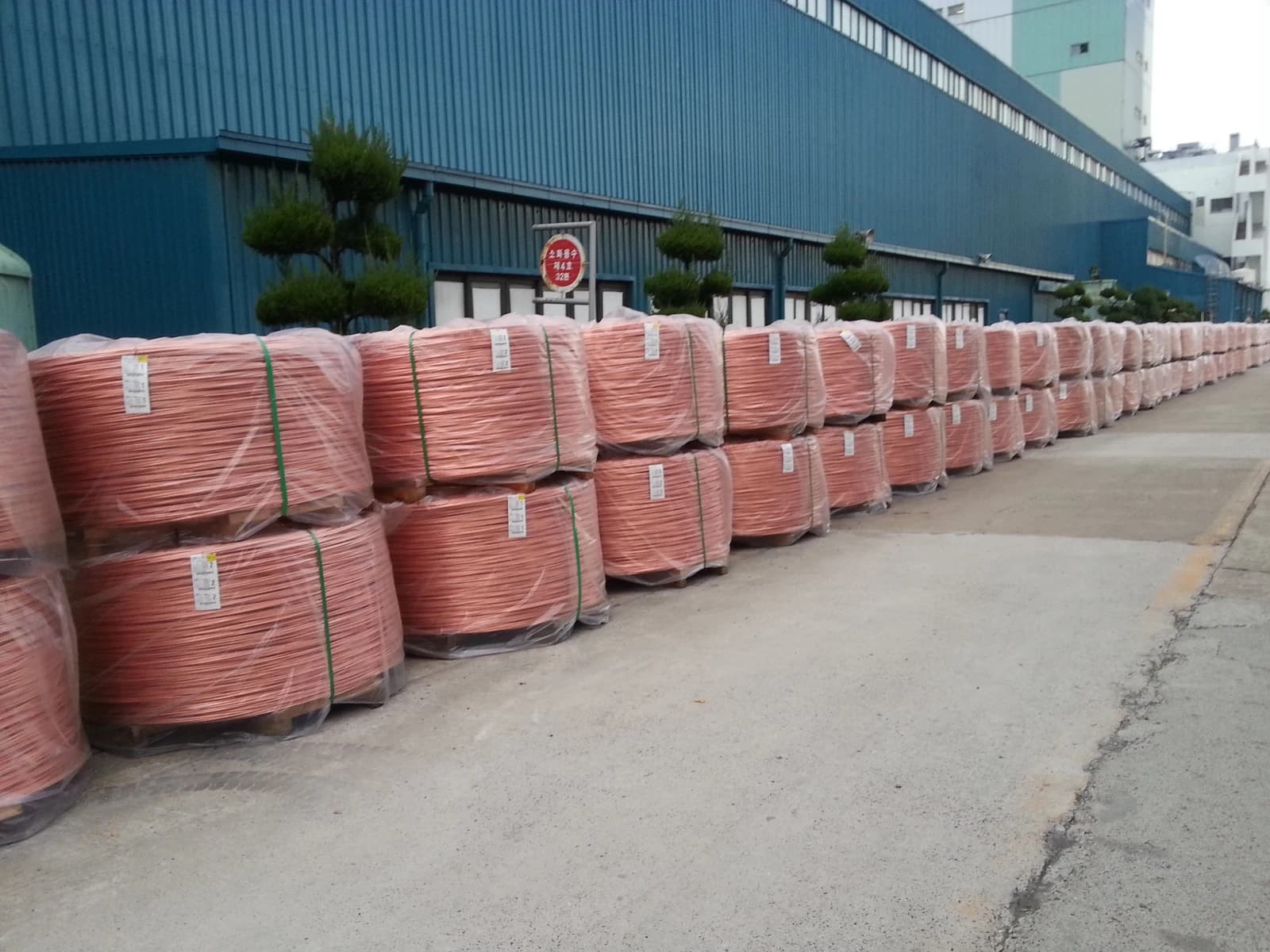Copper wire rod coils produced by LS Cable & System stacked outdoors next to a building.