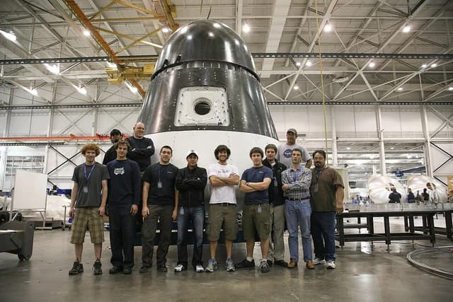 SpaceX engineers stand around a Dragon spacecraft qualification unit inside a facility.